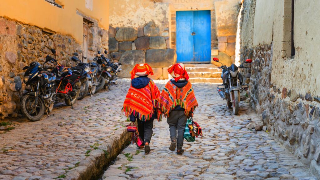 Niños en Ollantaytambo vistiendo trajes típicos y sonriendo frente a un paisaje andino.