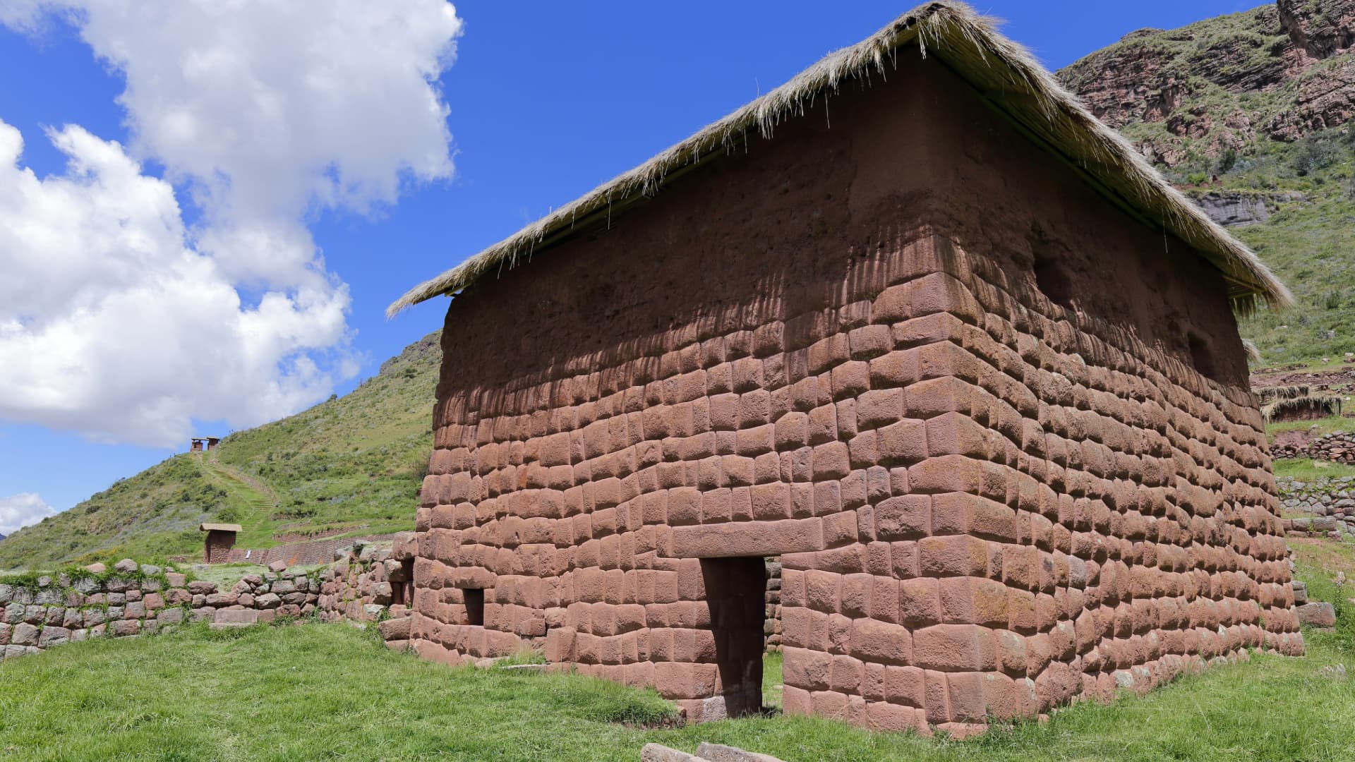 Arquitectura Inca: Descubre recintos en Huchuy Qosqo, Cusco Antigua construcción inca de piedra con techo de paja y puerta trapezoidal en el complejo arqueológico de Huchuy Qosqo, Perú.