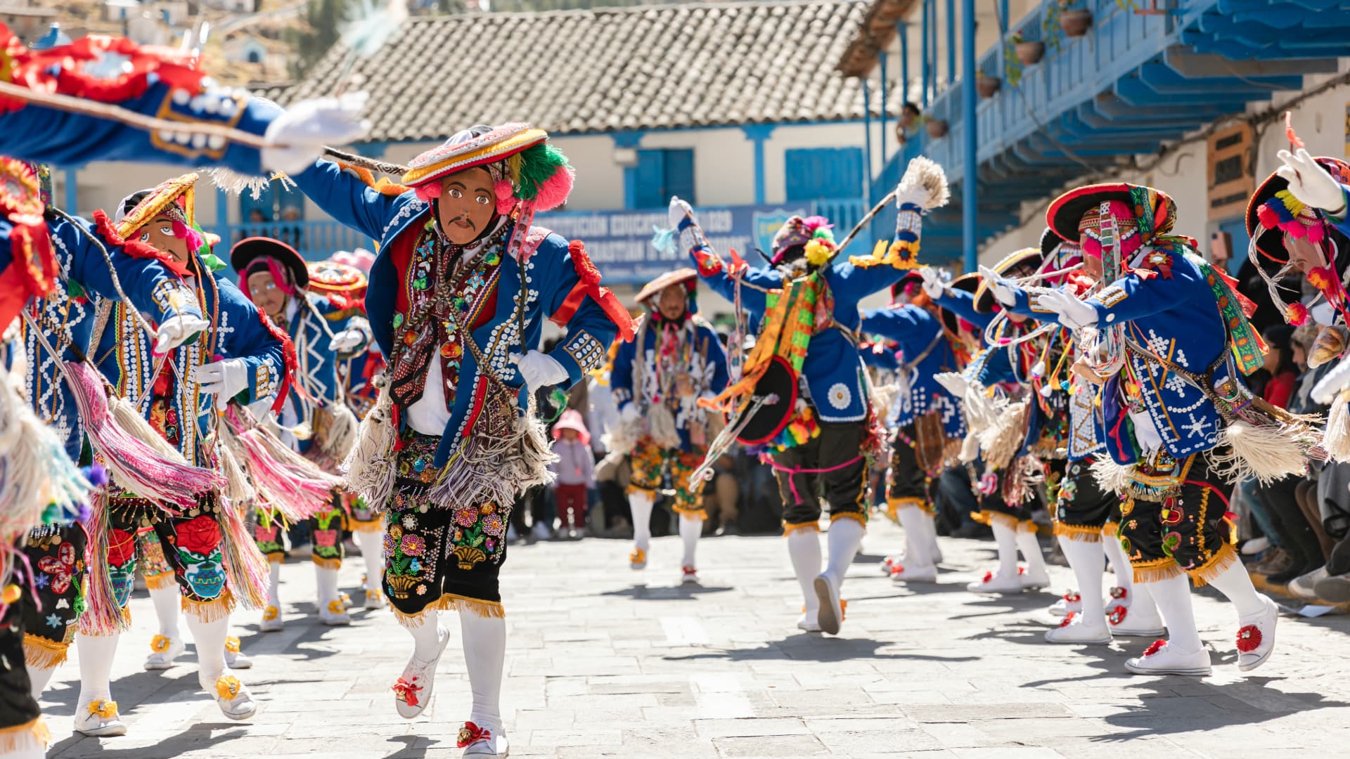 Danzantes Saqra con máscaras y trajes vibrantes bailando en las calles coloniales de Paucartambo durante la procesión de la Virgen del Carmen.