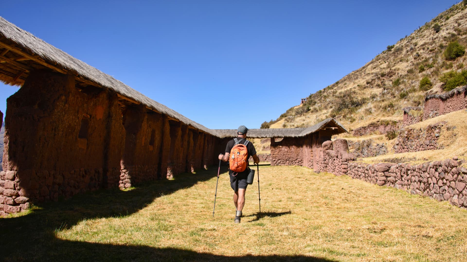 Explorando Huchuy Qosqo, Cusco Excursionista con mochila caminando entre los imponentes muros de piedra y adobe del sitio arqueológico inca de Huchuy Qosqo, Perú.