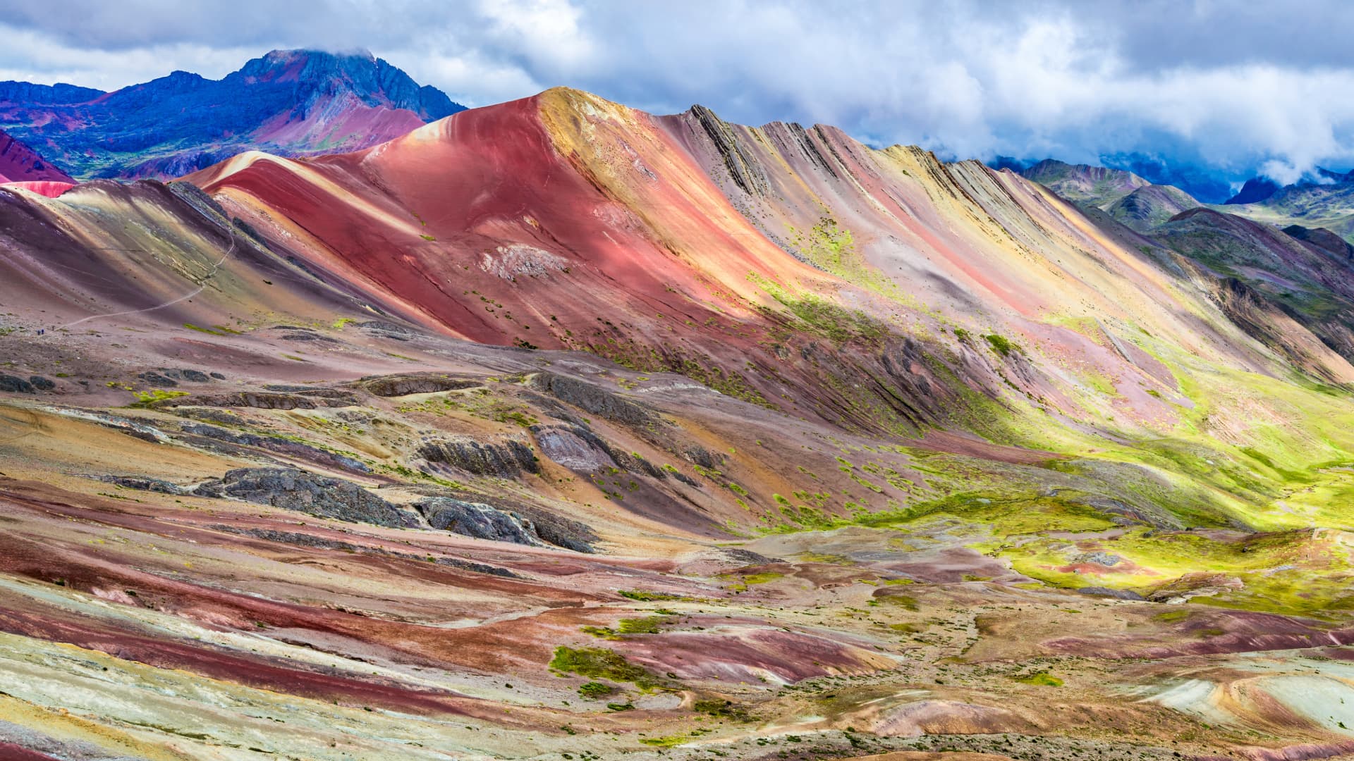 Tour a la Montaña de 7 Colores: Magia en Vinicunca Laderas de la Montaña Vinicunca revelando sus vibrantes franjas de colores minerales bajo un cielo dramático en Cusco.