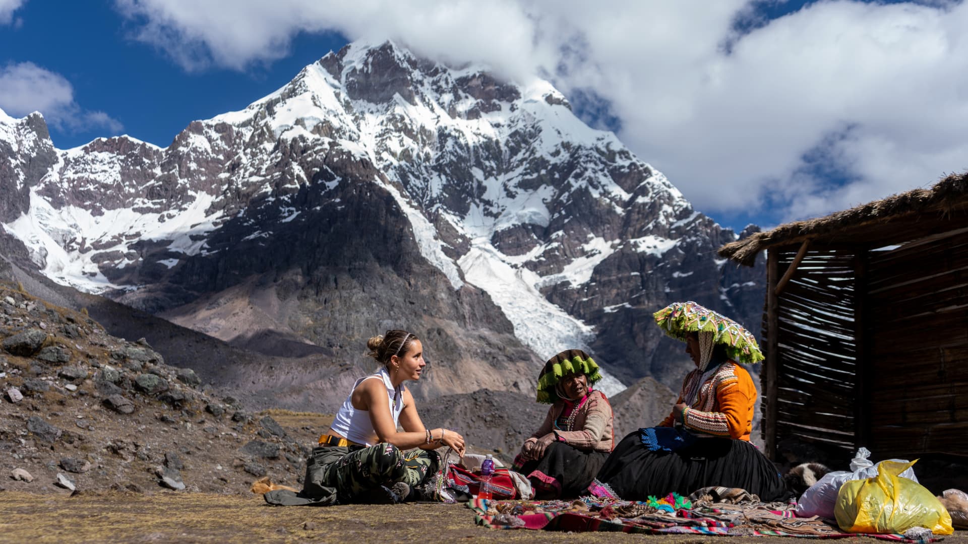 Turismo Vivencial en Ausangate: Conecta con su Gente Viajera conversando con dos artesanas andinas que muestran sus textiles tradicionales a los pies del Nevado Ausangate en Perú.