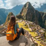 Una mujer joven con una mochila naranja sentada sobre una roca contempla la majestuosa ciudadela inca de Machu Picchu y la montaña Huayna Picchu.